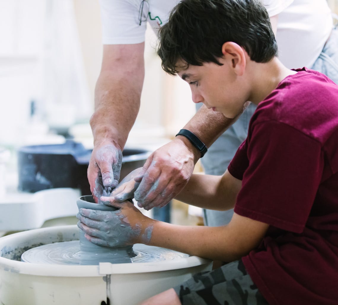Camper learning pottery wheel with instructor's help