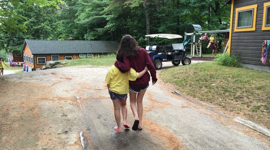 Camper and big sister walking with arms around each other's waists.
