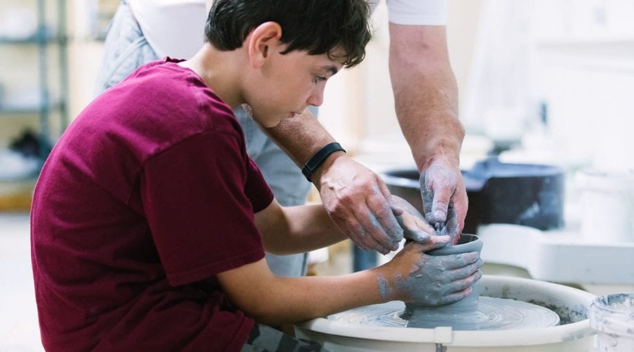 Boy learning how to use the spinning wheel in ceramics