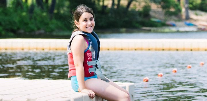 Girl with lifejacket on sitting on dock