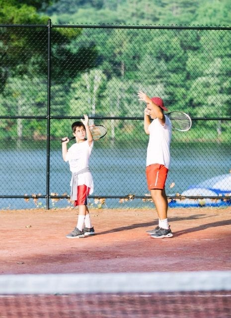 Staff teaching male camper tennis